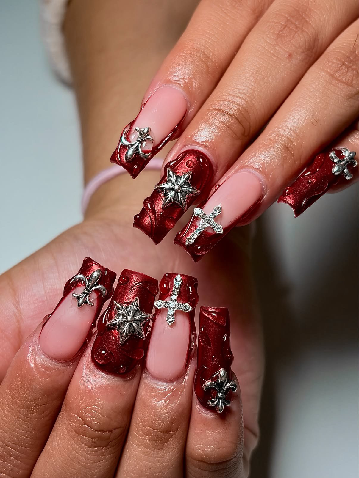 Deep red chrome Gel-X set with silver cross and fleur-de-lis charms